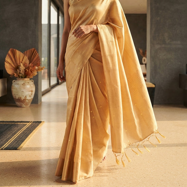 Close-up of a silk saree drape showing fluid, elegant folds on a woman in a sunlit, modern space.